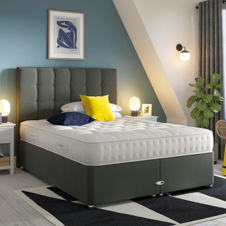 Grey upholstered bed with mattress uncovered in a blue bedroom