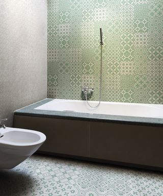 Patchwork bathroom tile ideas shown on a floor and wall behind a bathtub