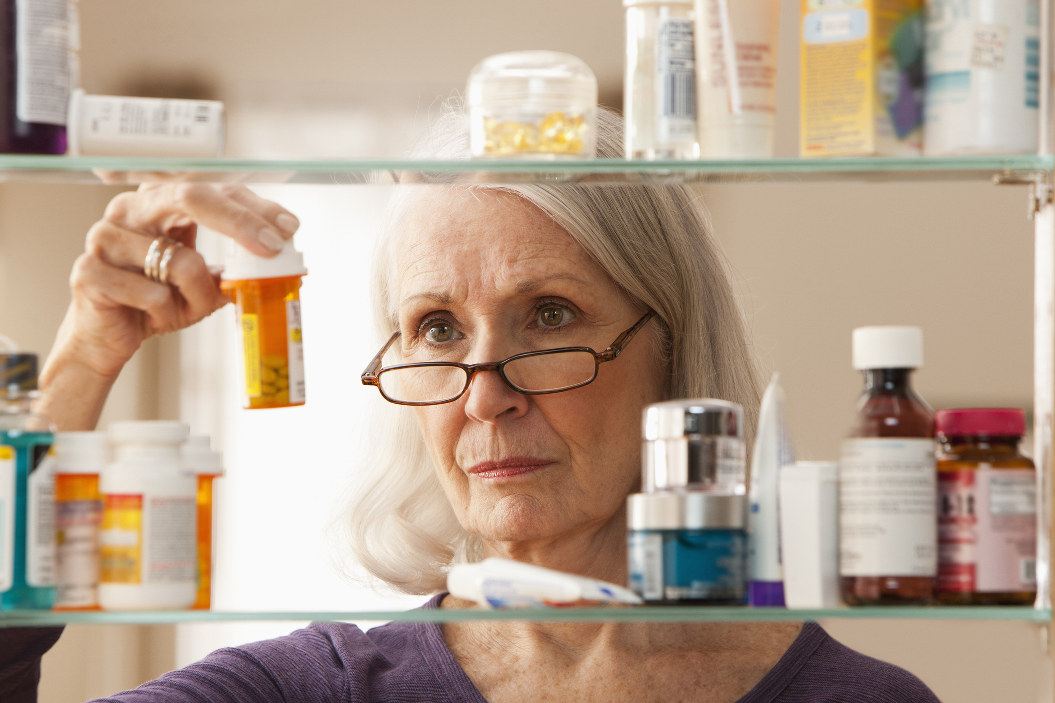 A mature woman inspects bottles of medication in her medicine cabinet.