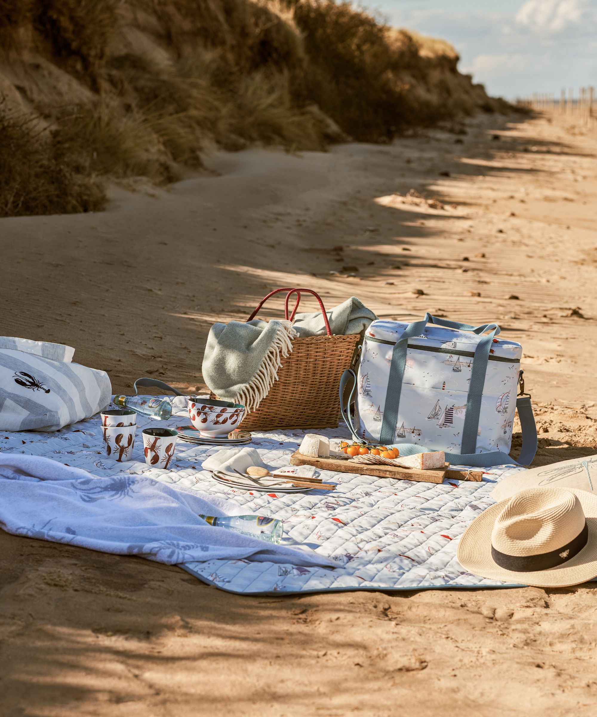 picnic blanket with beach bag and cool bag on a sandy beach