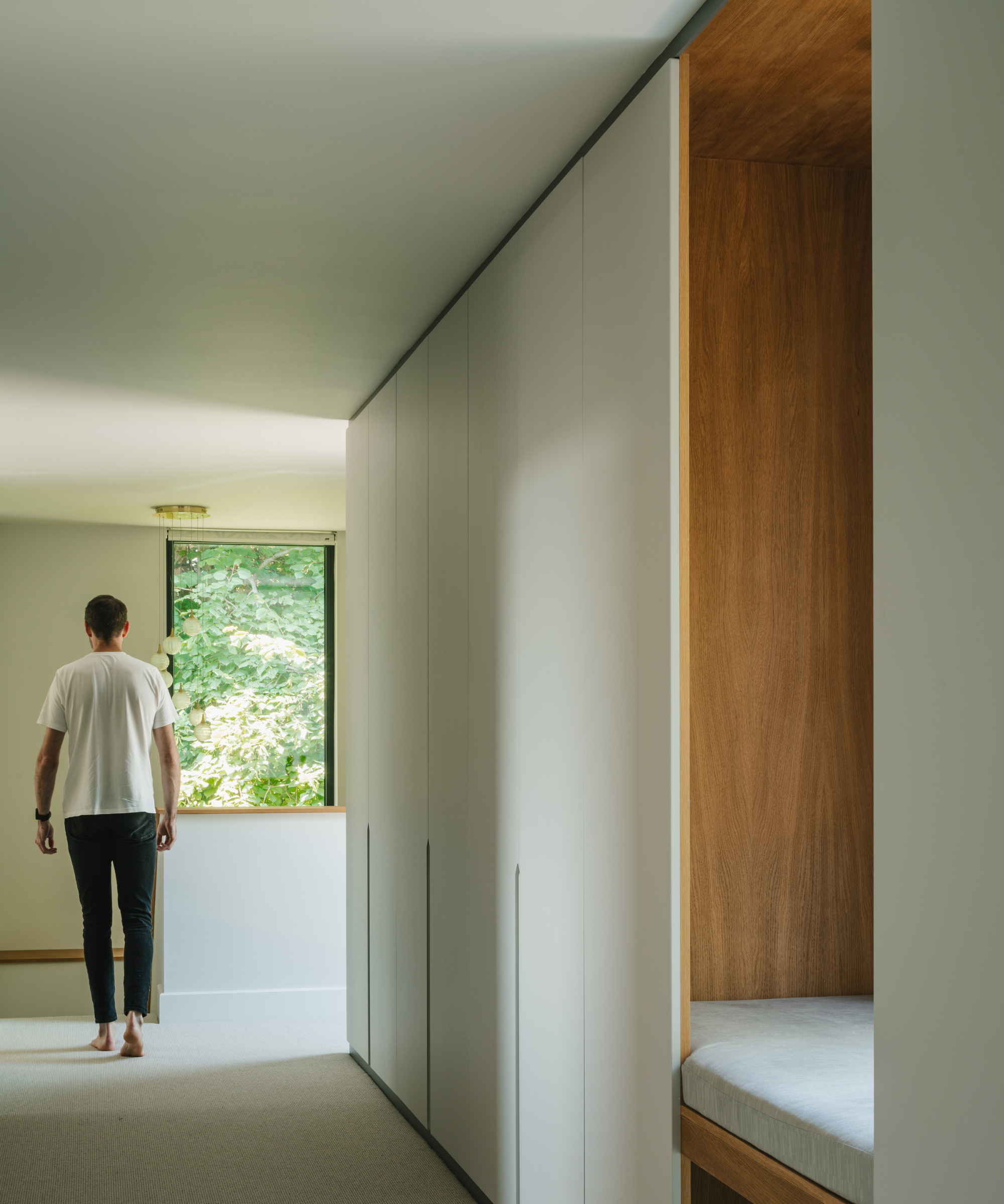 Person walking in hallway with window straight ahead and window seat to right hand side