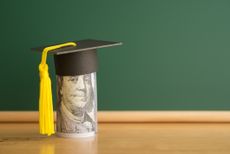 Hundred-dollar bill with a graduation cap on top and a green chalkboard in the background