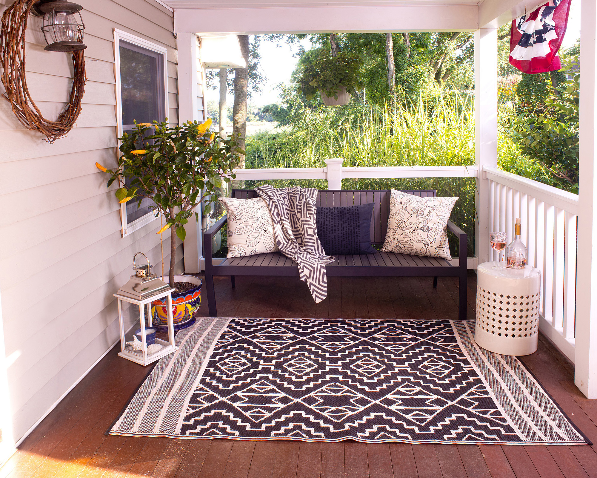 A decking idea in front porch with patterned outdoor rug, monochrome chairs