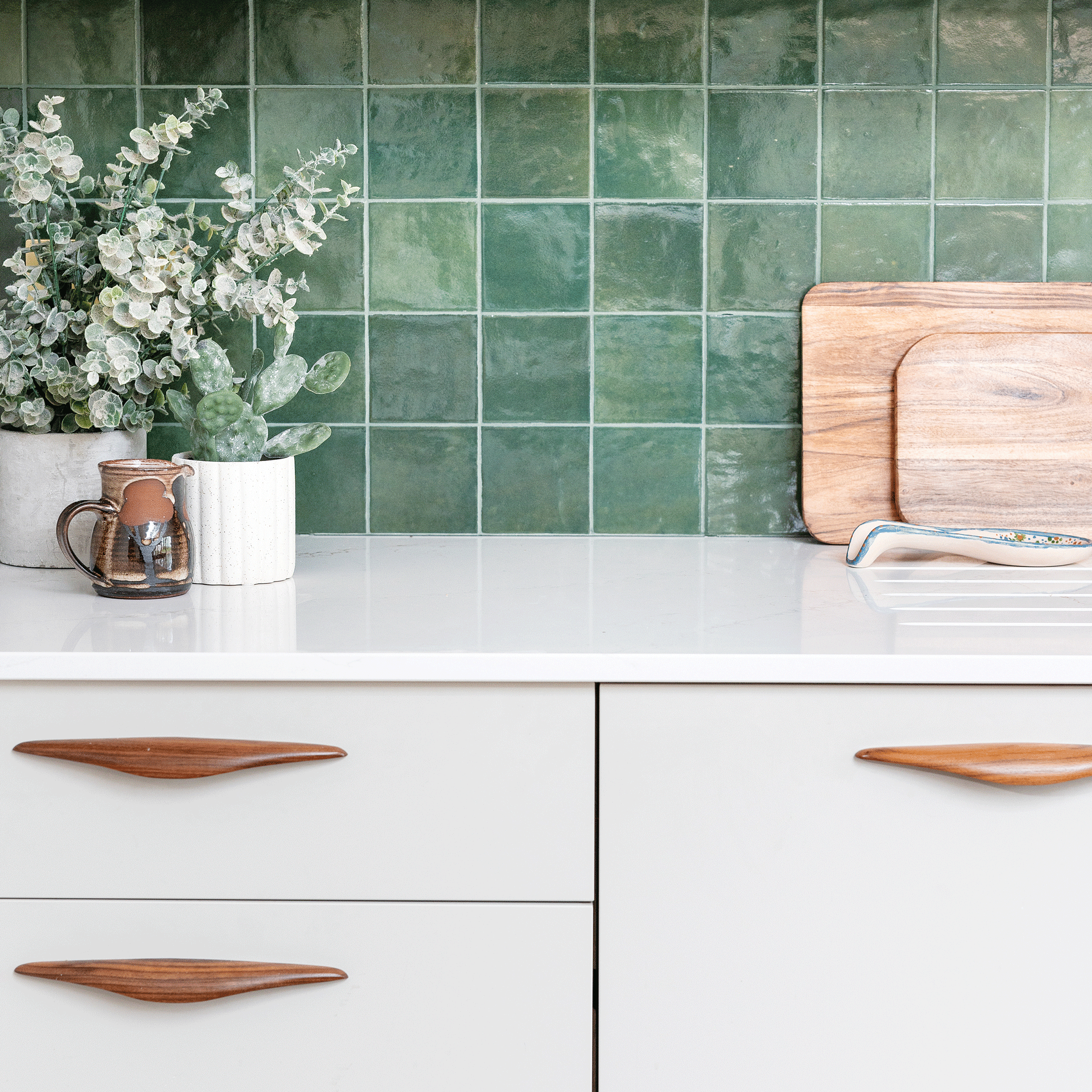 a kitchen with a green tiled splashback and white cabinets with retro wooden handles