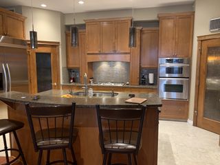 A dated kitchen with dark wooden cabinetry, granite countertops, and tiled flooring