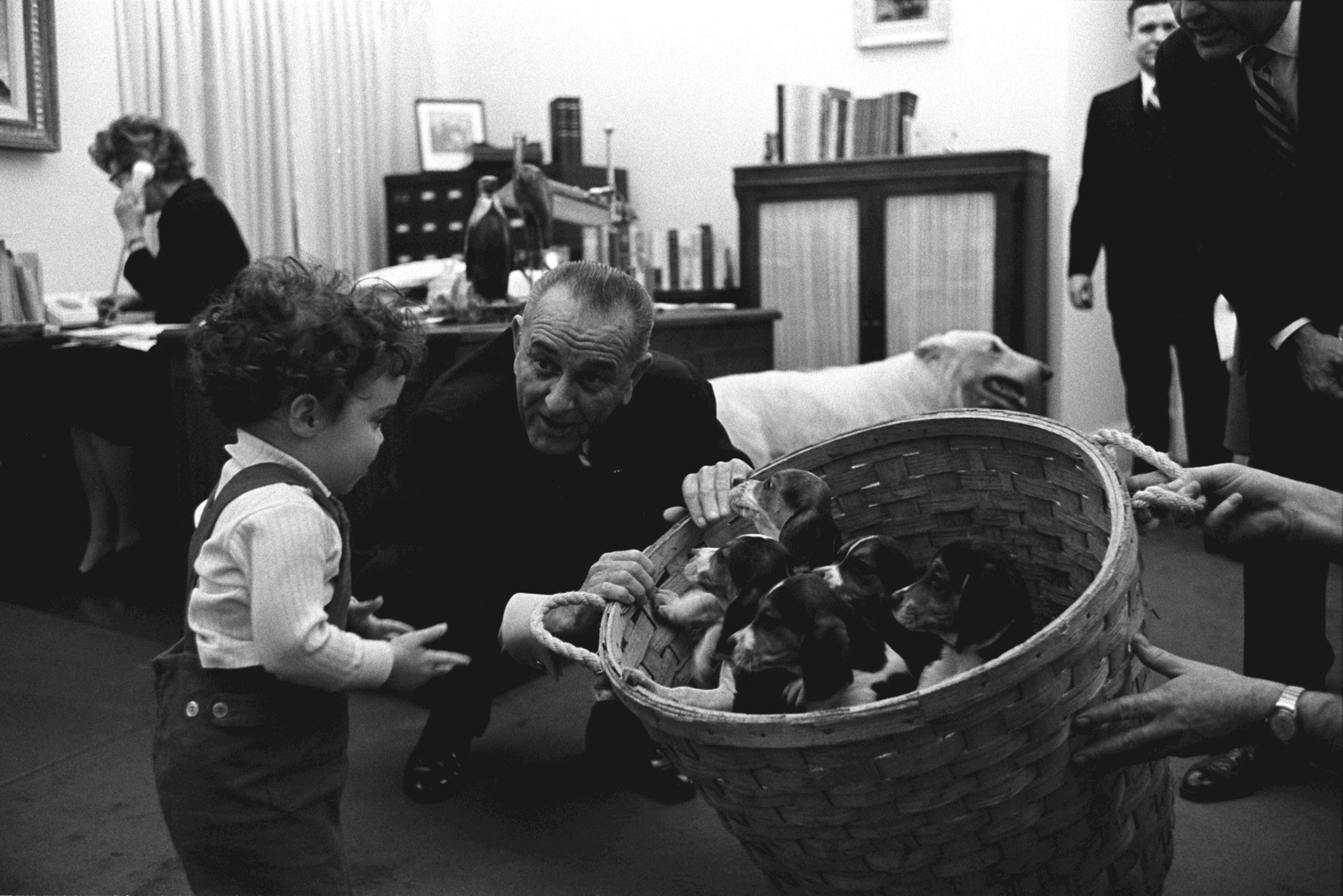 Lyndon B. Johnson shows a basket of puppies to an excited boy in the Oval Office.