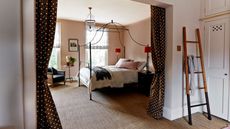 A peach bedroom with a black four-poster bed, polka dot curtains, and a blanket ladder against a linen closet.