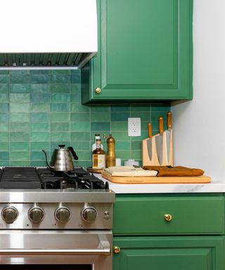 A kitchen with a silver stove, bright green cabinets, and blue and green tile backsplash