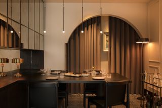 A dining room table with pendent lighting, a mirror and curtains