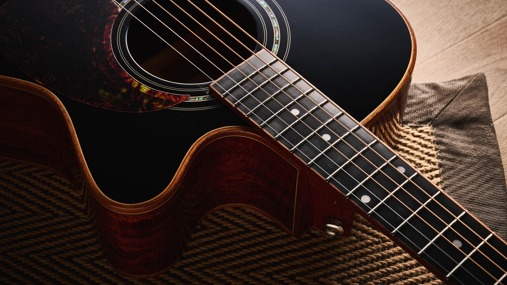 Harley Benton CLC-650SM-CE: the affordable cutaway electro-acoustic has a black top, natural back and sides, with an attractive arm-rest and tortoiseshell pickguard, and is here photographed against a wooden floor.