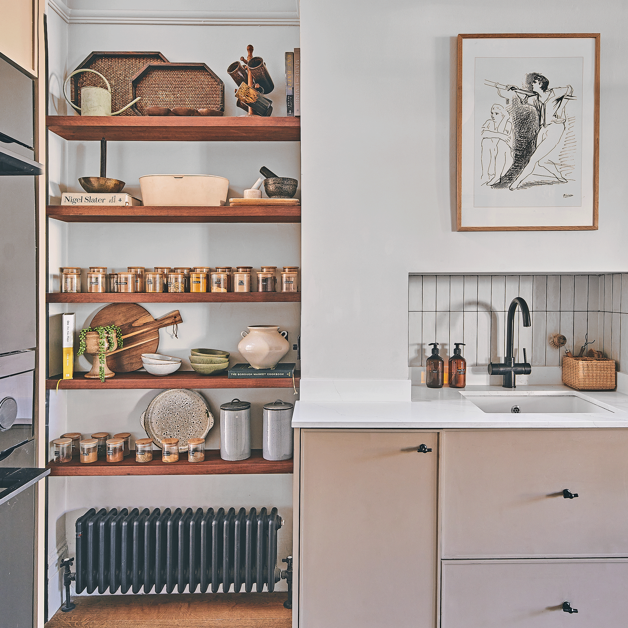 a kitchen with beige cabinets and a kitchen sink beside a set of open alcove shelves storing a variety of kitchen accessories including matching decanted spice jars