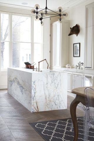 a marble kitchen island in a white kitchen with large patio doors and dining area