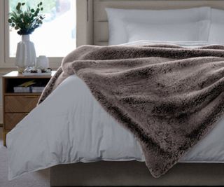 Luxe Faux Fur Throw on a white comforter against a wood wall.