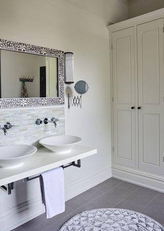 Bathroom with countertop and double sinks, mirror above, closet, neutral wall and gray floor