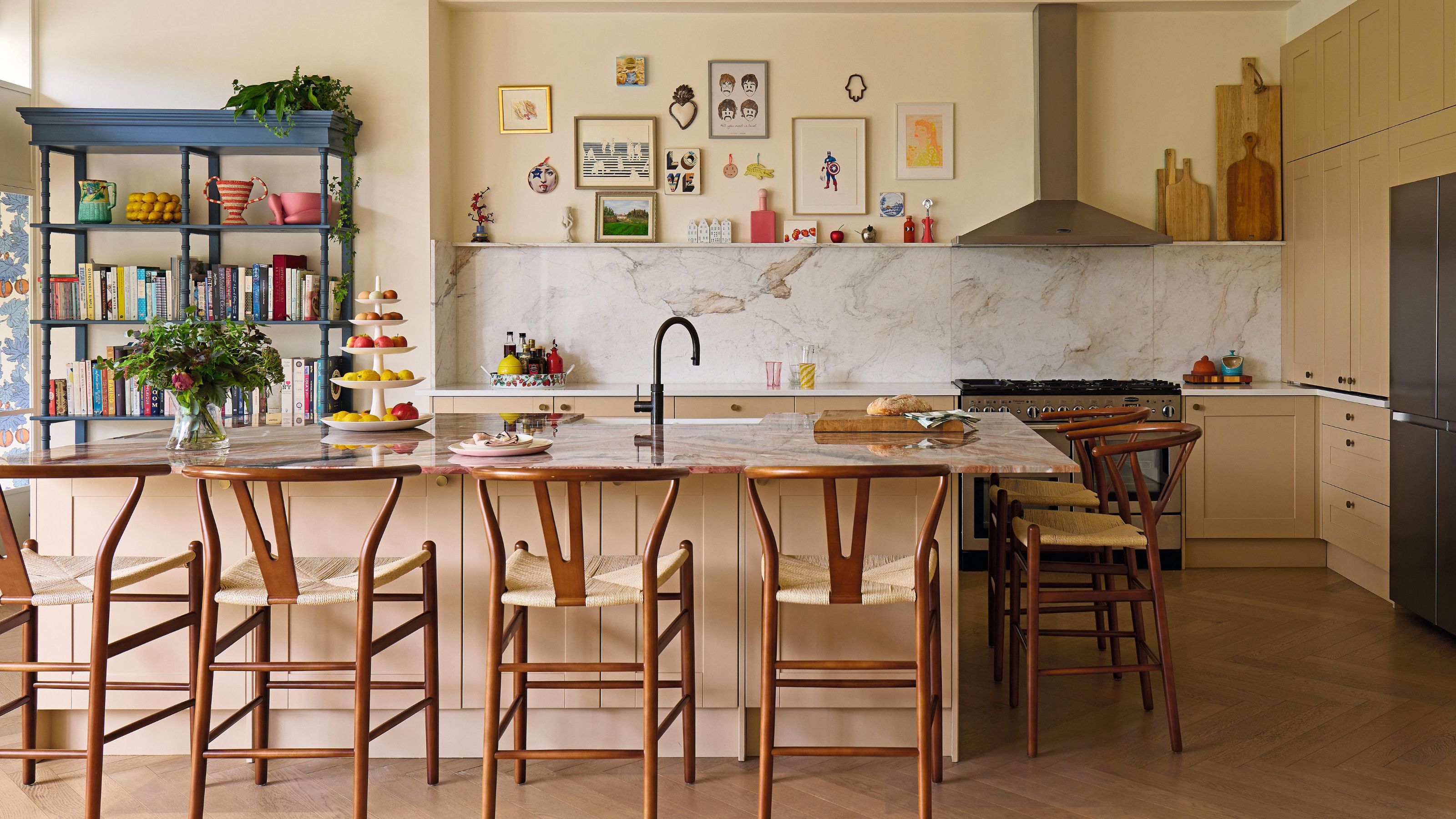 a warm yellow neutral kitchen with a large island with wooden bar stools and a gallery wall above the kitchen backsplash