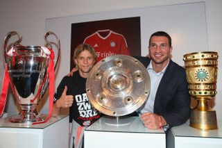 Former Bayern Munich player Anatoliy Tymoshchuk and boxer pose with trophies won by the German club in 2013.