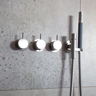 Stainless steel thermo mixer, diverter and handshower on large grey bathroom tile decor
