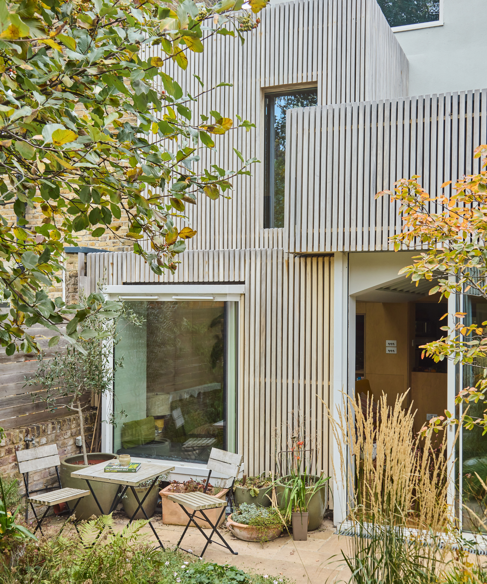 Exterior of a wooden cladded house with a patio out of the front with table and two chairs