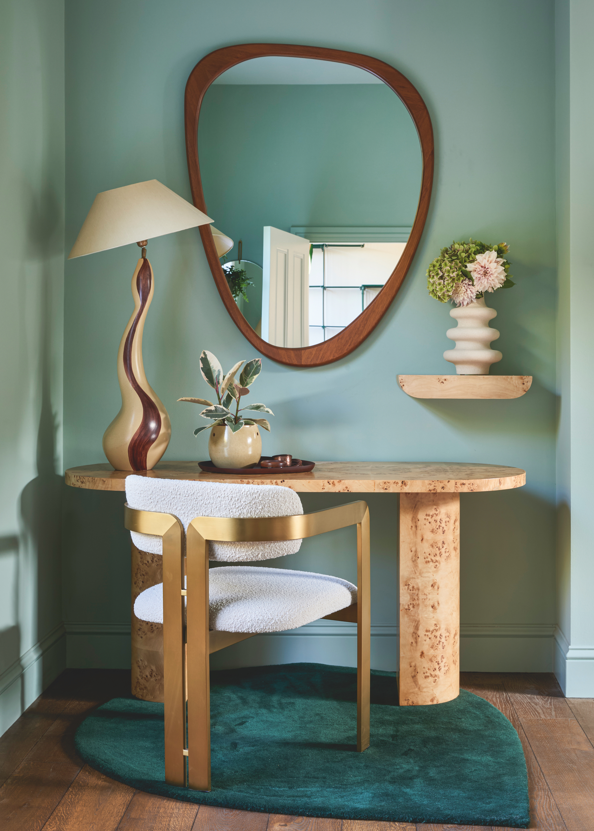 Turquoise walled dressing area with oval mirror, with curved vanity table and blue and gold arm chair.