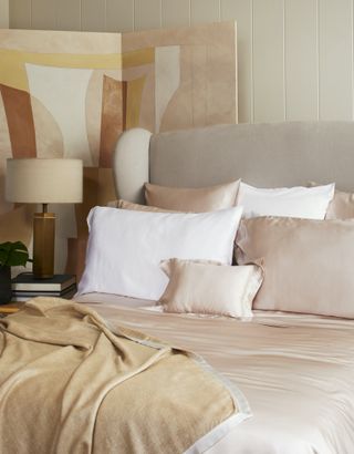 neutral bedroom with silk bedding, ochre blanket, painted screen, table lamp
