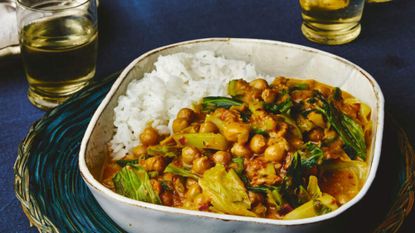 Spring greens and chickpea curry served in a white bowl, on a blue tablecloth