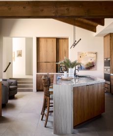 Cozy dark wood kitchen with wooden beams, cabinetry. Wood and marble island with wooden stools.
