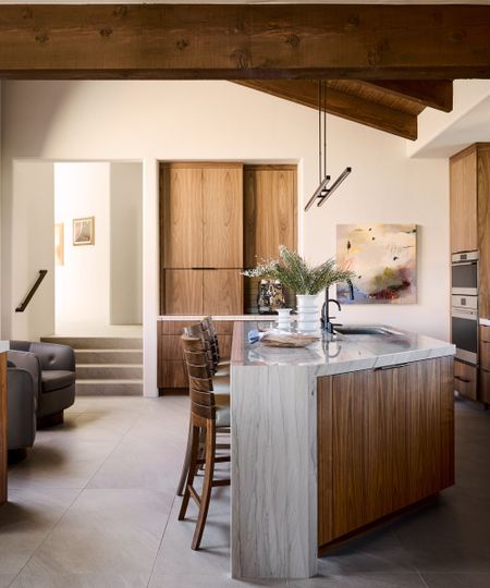 Cozy dark wood kitchen with wooden beams, cabinetry. Wood and marble island with wooden stools.
