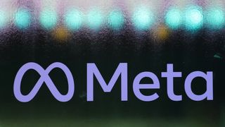 The Meta logo (a stylized &#039;M&#039; next to the word &#039;Meta) written in blue on a frosted glass window, with blue lights visible behind the glass.