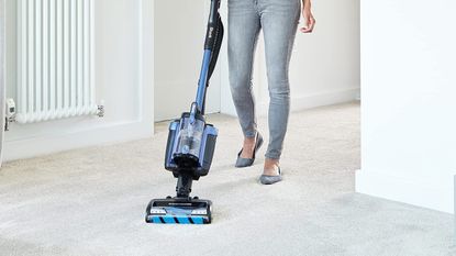 woman using Shark vacuum on carpet, to illustrate w&h's best vacuum guide
