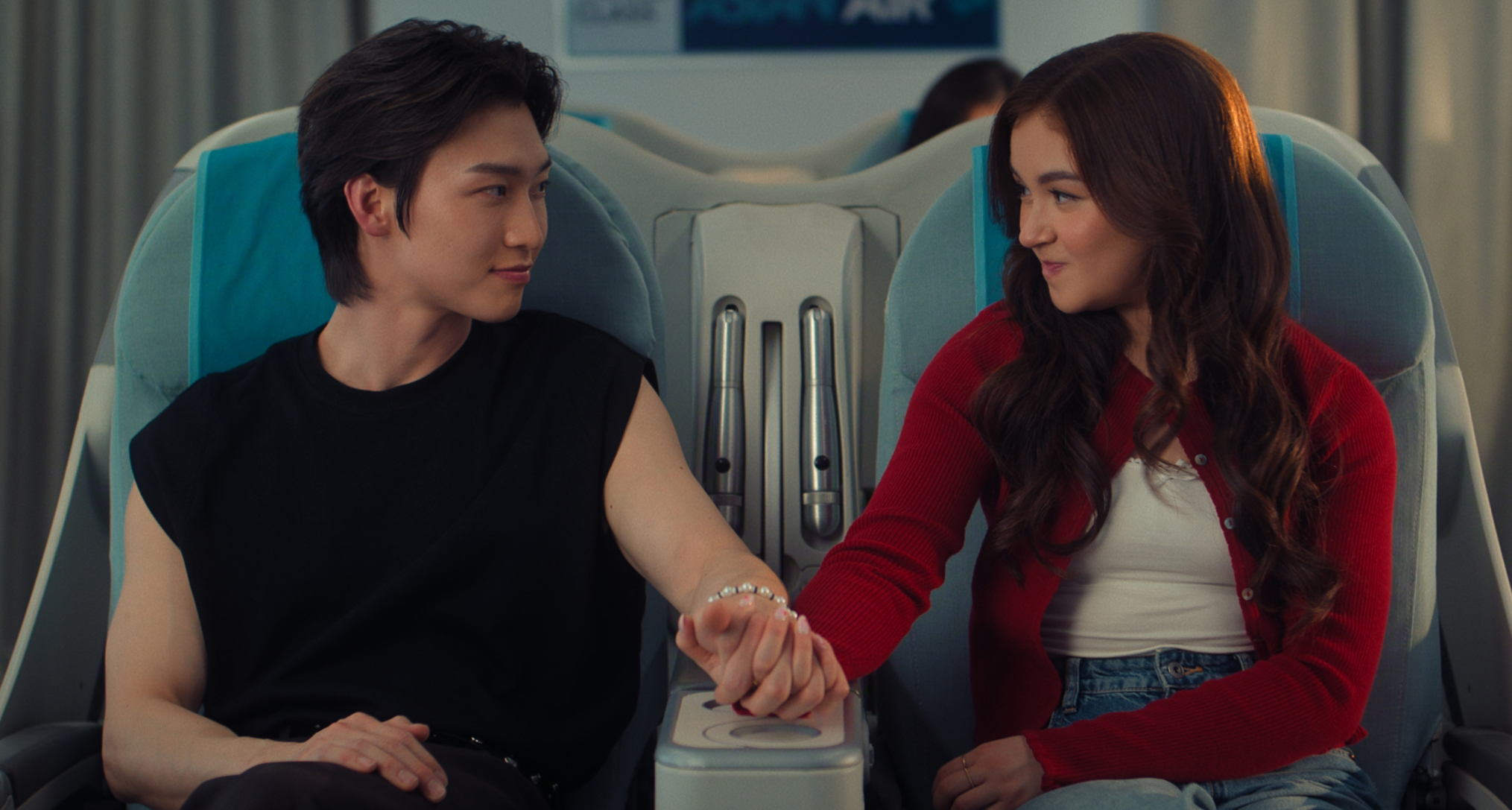 kitty covery song and min jo hold hands on a flight together before it takes off in a still from the xo kitty season 3 finale