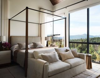 A bedroom with a view and large windows. Sheer curtains hang on the left side of the room. A sofa sits at the foot of the bed