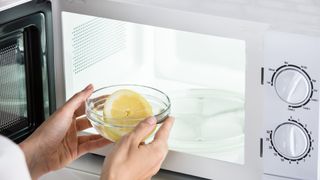 Woman placing bowl of lemon and water inside microwave