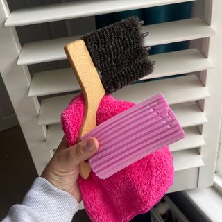 Hand holding a blind cleaning brush, a duster, and a Damp Duster in front of plantation shutters