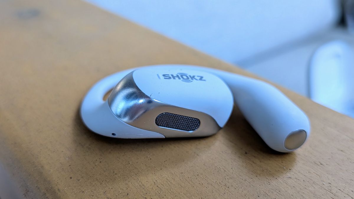 A close-up of a single Shokz OpenFit 2+ earbud, focused on the speaker grill on the bottom that angles into your ear.