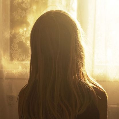 a person with long hair looking out a window