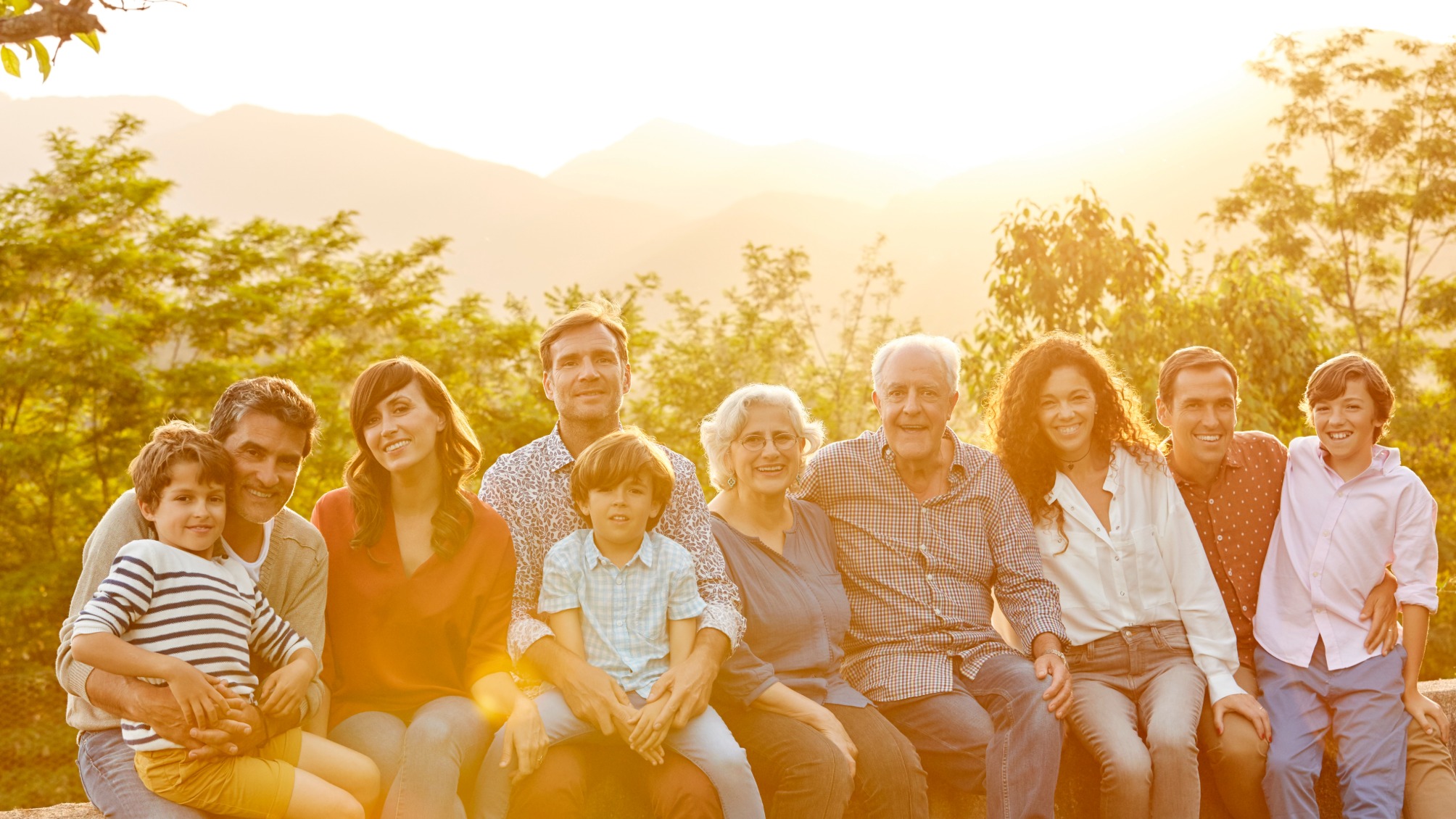 Portrait of happy multi-generation family sitting on garden wall. 