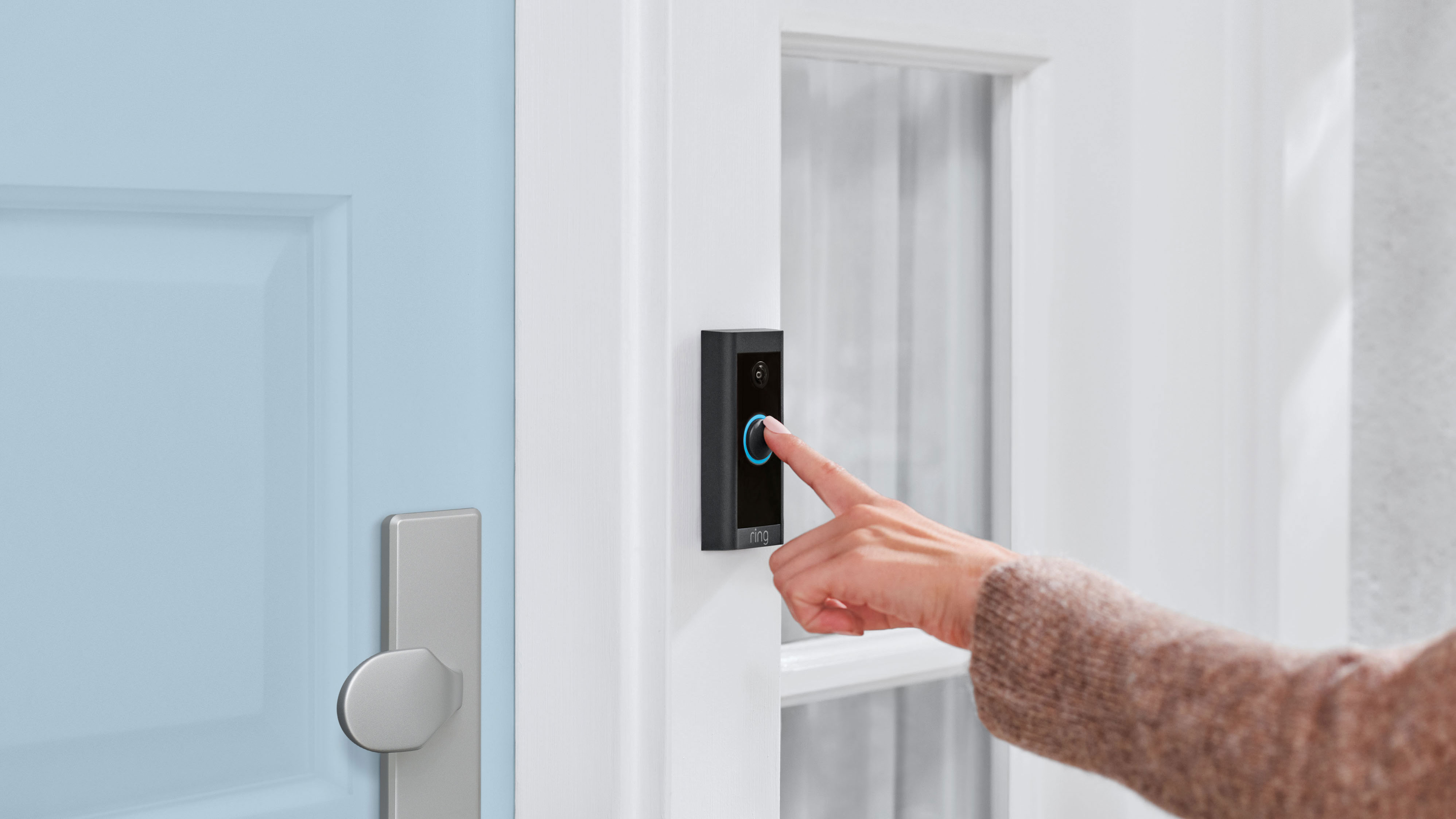 En person som ringer på en svart Ring Video Doorbell Wired som sitter monterad bredvid en blå dörr.