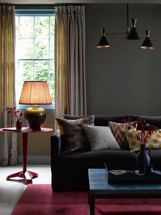 layered lighting in a cozy den with dark velvet sofa covered in cushions and red rug