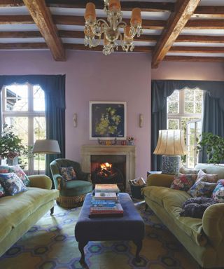 lilac living woom with original wooden beams and green velvet sofa and fire