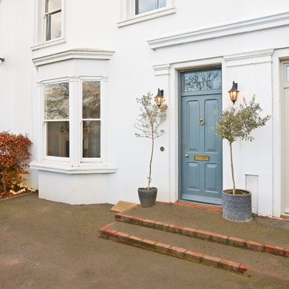 white house exterior with blue front door, wall lights and plants