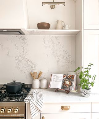 A white kitchen with a gold stove and a white countertop with books, plant, and utensils on top of it