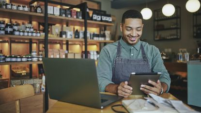 A small business owner smiles as he looks at his tablet in his deli shop.