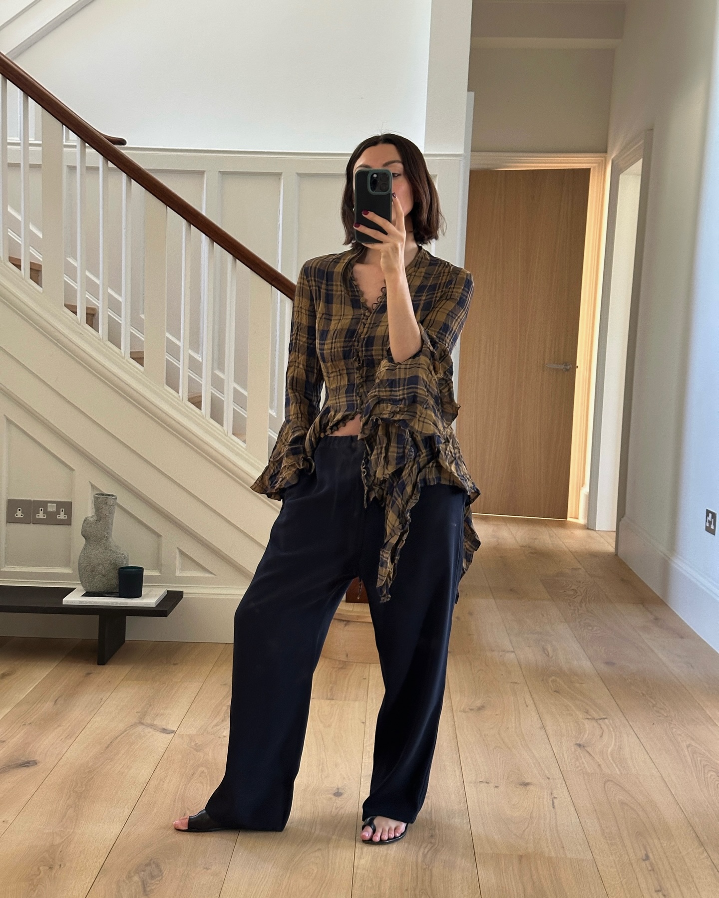 A woman wears a plaid top, black trousers, and toe sandals.