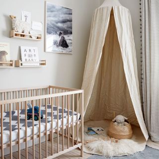 Nursery nursery with pale wood cot and beige canopy hung in the corner of the room