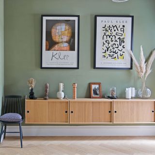 Wall-hung wooden storage unit against green wall with Paul Klee prints above