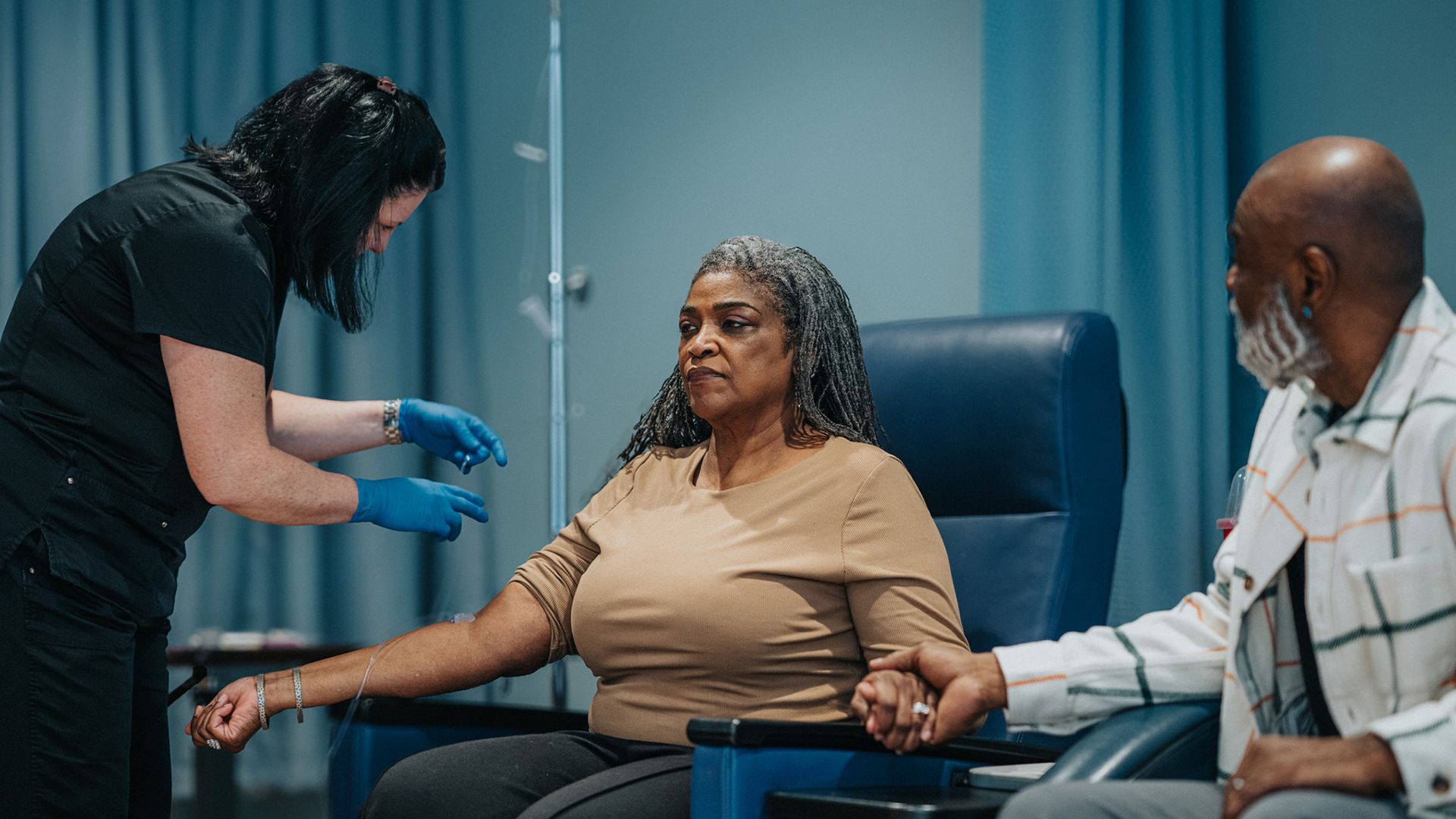 A woman sitting in a medical chair receives an IV.