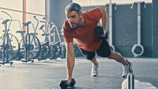 Mature man performing plank dumbbell row in gym