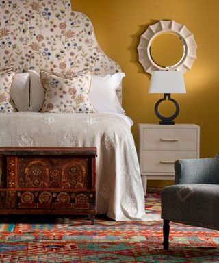 bedroom with yellow walls, floral patterned headboard, red vintage patterned rug and linen bedding