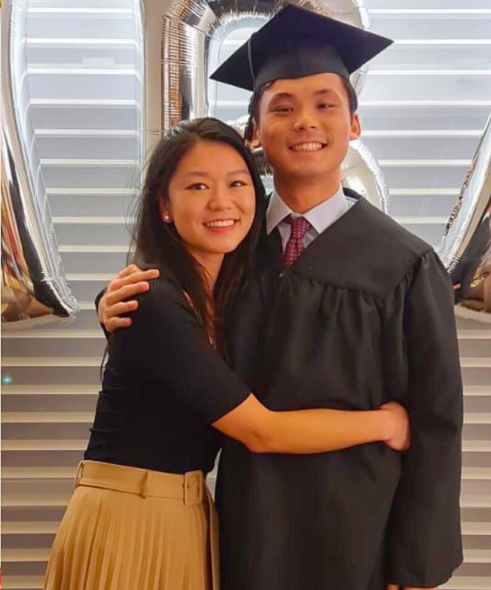Tania left, and her late brother, Tim, after his graduation. He is wearing a black cap and gown, and she is in a black top with pleated mustard skirt. They have their arms around each other and are smiling in this vibrant, happy, photo.