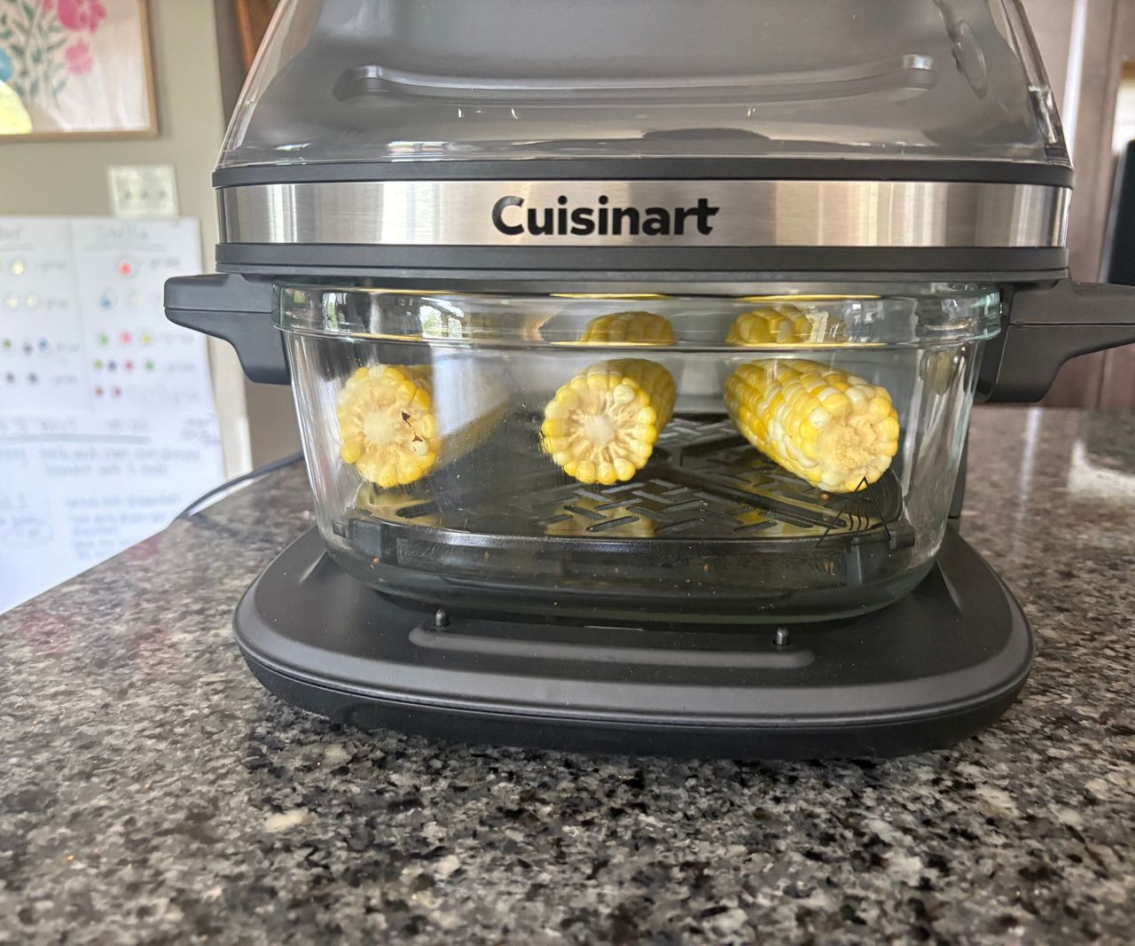 The Cuisinart glass air fryer on a granite countertop viewed from the side with three corn cobs inside.